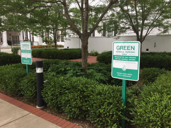 Área paisagística com placas de estacionamento para veículos ecológicos em frente a um edifício branco